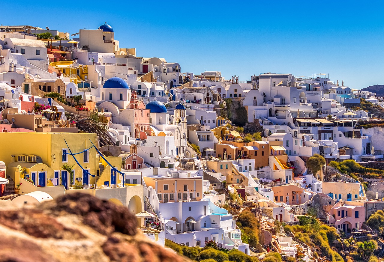 White-washed buildings with blue domes and vibrant flowers in a sunlit Santorini town.